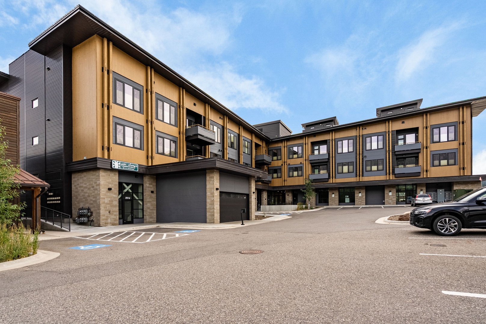 This modern mountain-style property features warm wood and stone accents, with convenient on-site parking at the entrance. The building's contemporary design includes multiple levels and balconies set against a scenic backdrop.