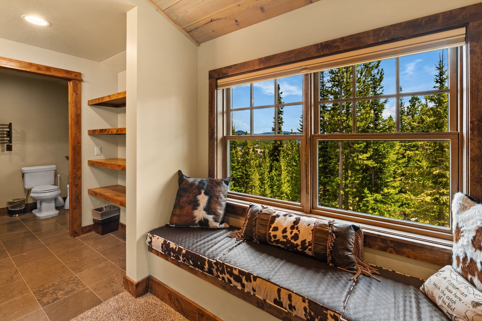 Curl up on the cozy window seat with your favorite book and enjoy stunning forest views through expansive windows, while rustic wood accents and thoughtful shelving add warmth and charm to your retreat.
