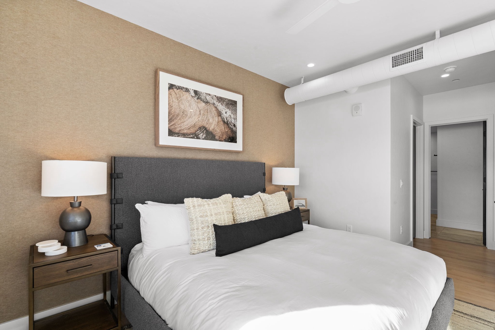 Sink into your plush king bed with crisp linens and textured pillows. Natural light fills your modern retreat with warm wood accents.