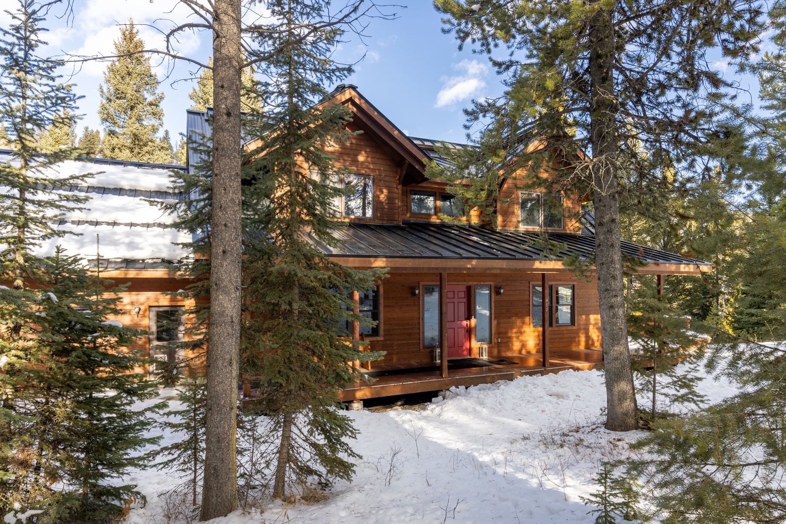 Charming mountain cabin nestled among evergreen trees with warm wood siding and a welcoming red door in a snowy forest setting.