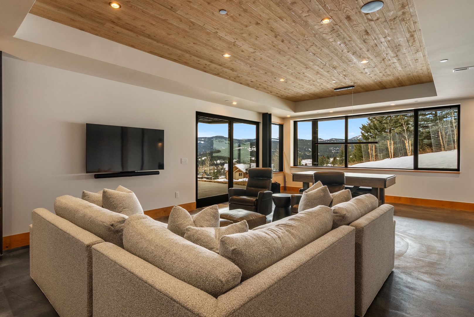 Unwind in your spacious living room where warm wood ceilings meet panoramic mountain views through floor-to-ceiling windows.