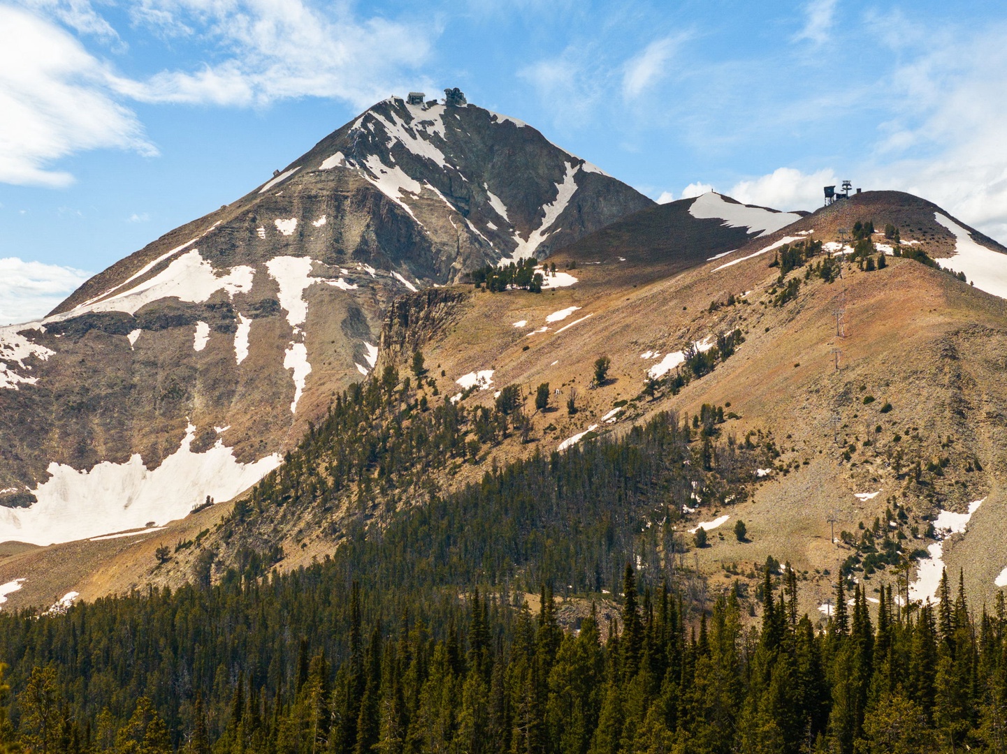 Dramatic mountain peak with patches of late-season snow rises above forested slopes, marking the natural landscape surrounding the property.