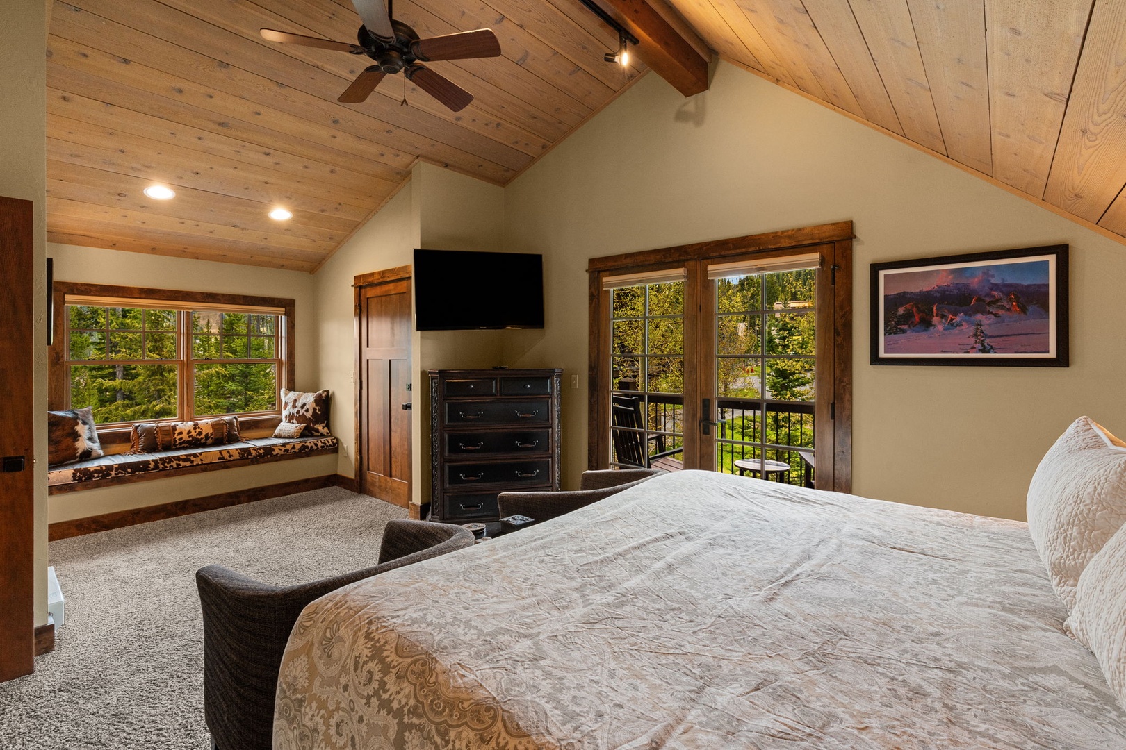 Relax in this inviting bedroom featuring a cozy bed, vaulted wood ceilings, and a private balcony with serene forest views. Your perfect mountain retreat awaits.