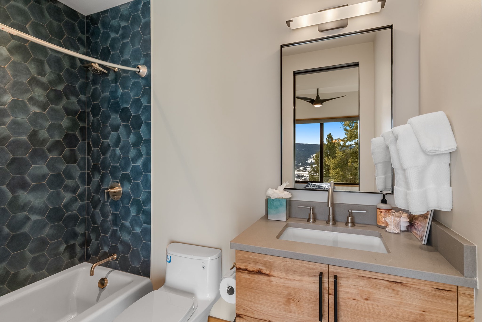 Your modern bathroom features stunning teal hexagon tiles, a relaxing soaking tub, and fresh mountain views through the window.