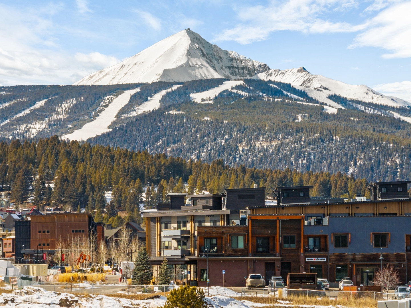 Modern mountain town nestled beneath snow-capped peaks with pristine ski slopes and alpine forests creating a stunning winter backdrop.