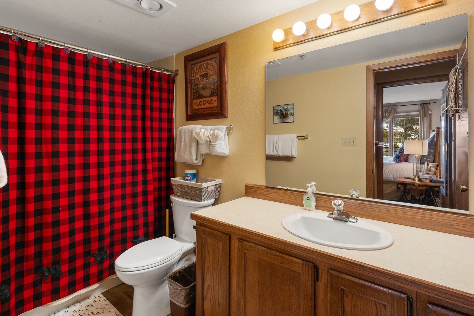 Your cozy bathroom features warm lighting and rustic charm with cheerful red plaid accents to brighten your morning routine.