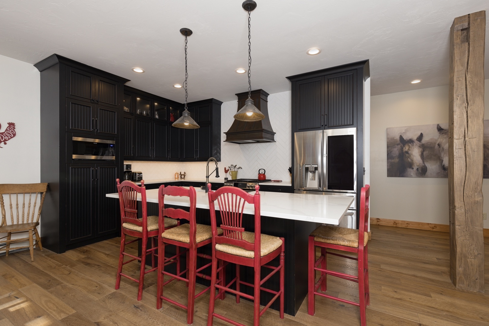 Gather around your spacious kitchen island featuring charming red bar stools, dark cabinetry, and rustic wood beams creating the perfect farmhouse feel.