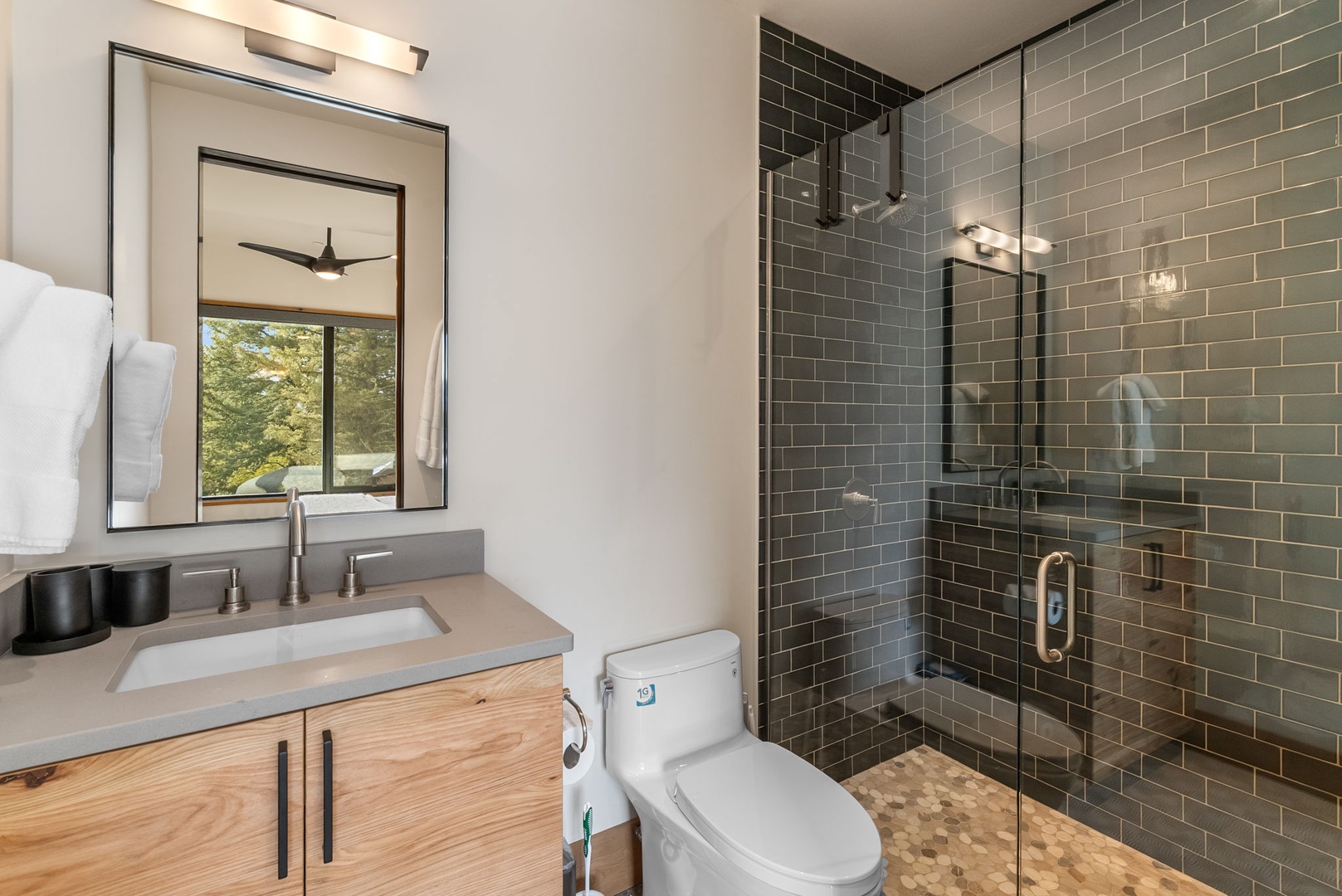 Refresh in your modern bathroom with elegant subway tile shower, natural wood vanity, and peaceful forest views.