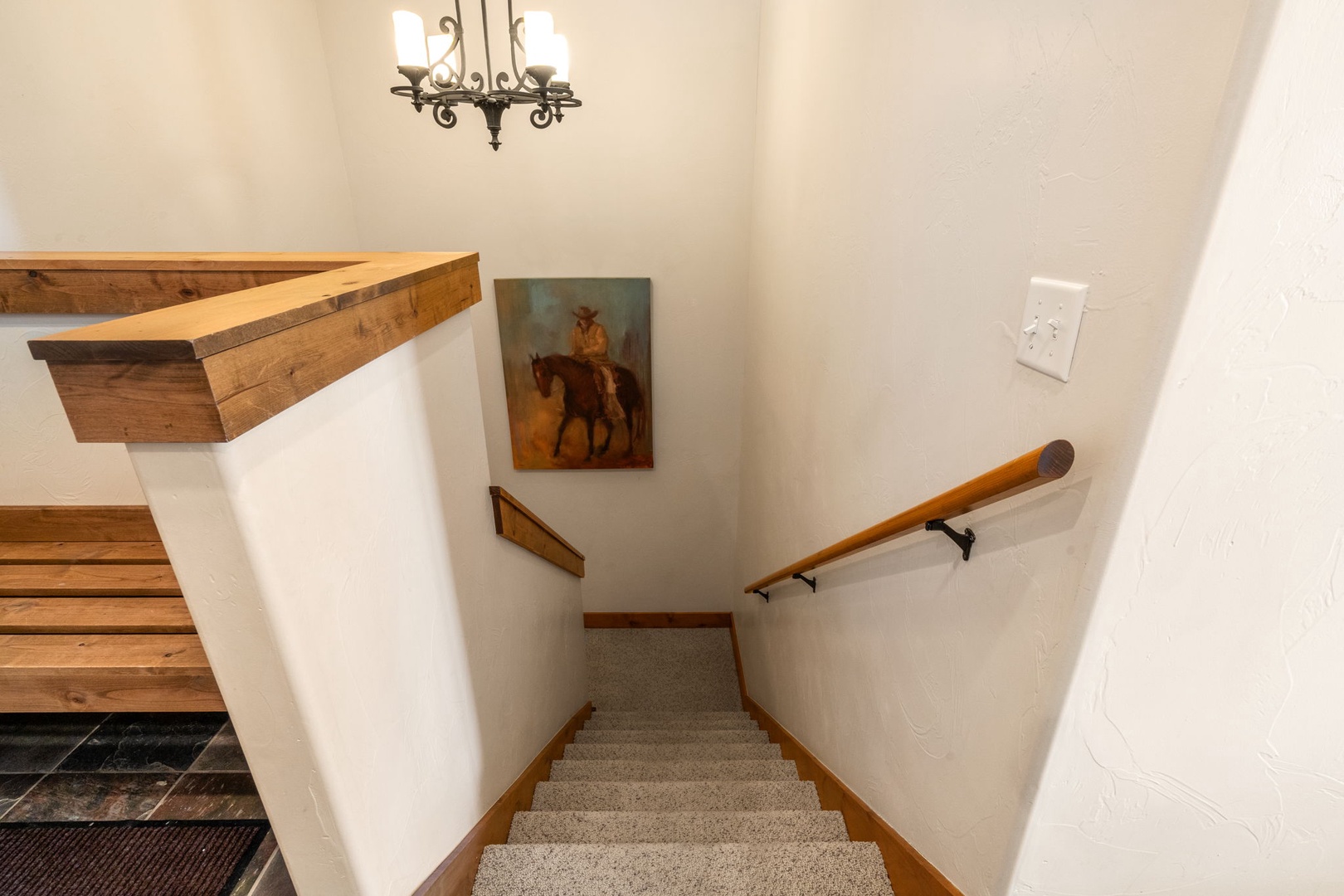 Navigate between floors with ease on these well-lit carpeted stairs, featuring warm wood railings and charming equestrian artwork.