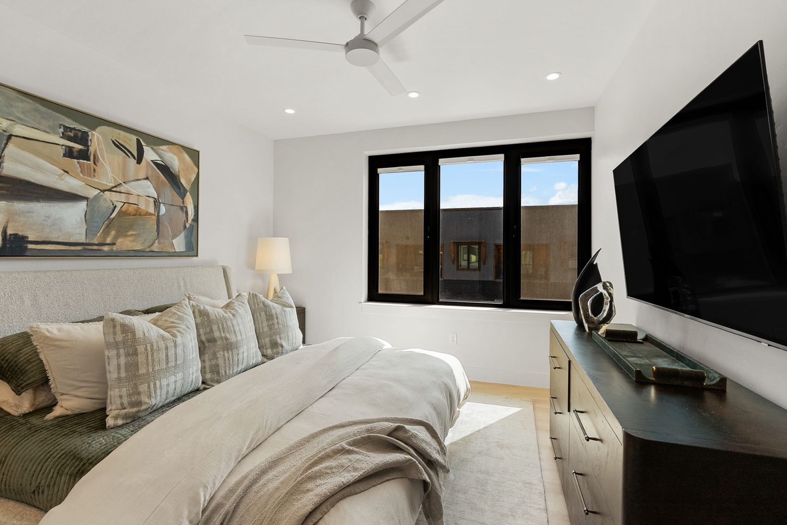 Sink into plush bedding with modern art above and your own flat-screen TV for cozy evenings in. Natural light fills the space through sleek black-framed windows.