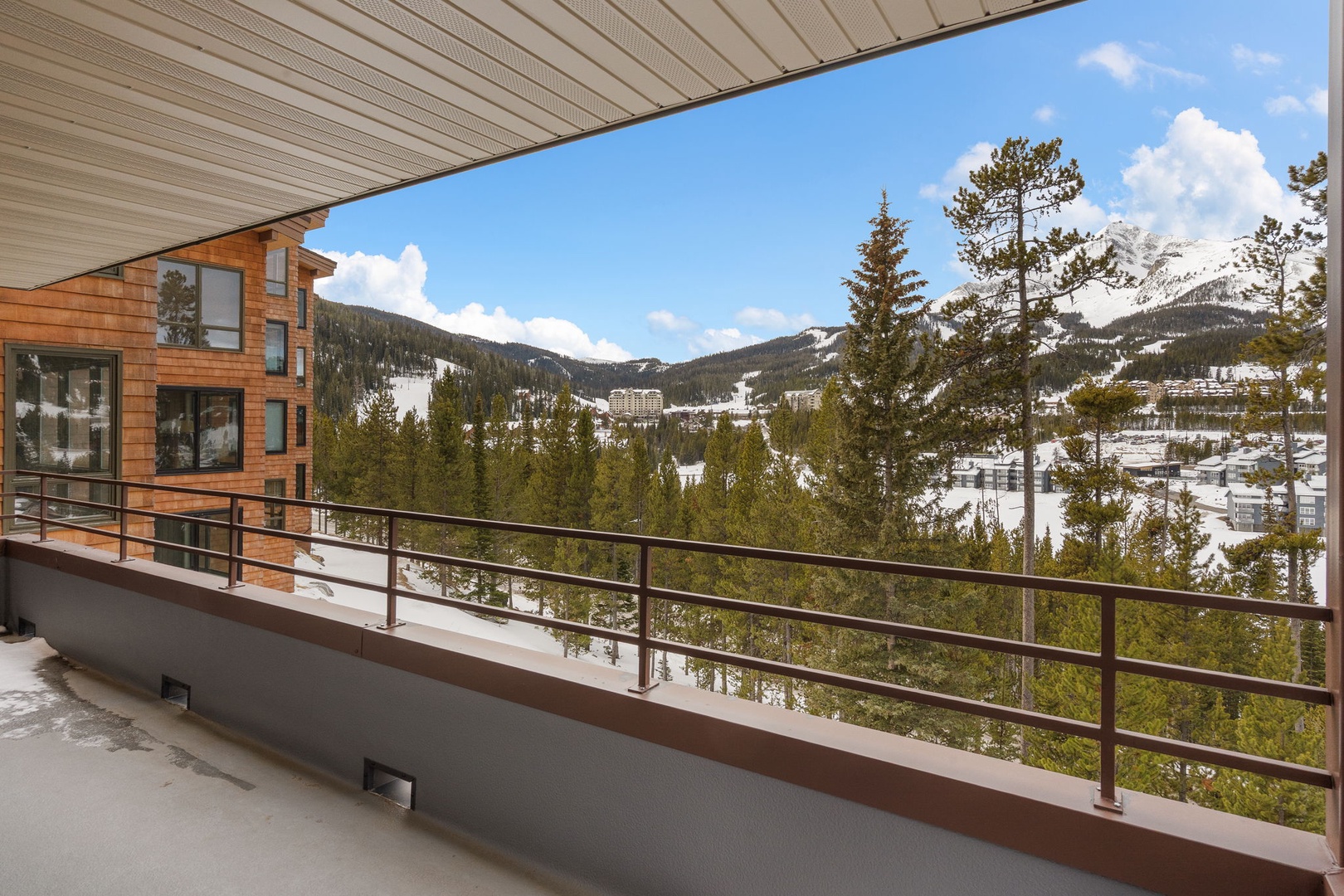 Spectacular mountain vistas unfold beyond this covered balcony, showcasing snow-capped peaks and forested valley views in a peaceful alpine setting.