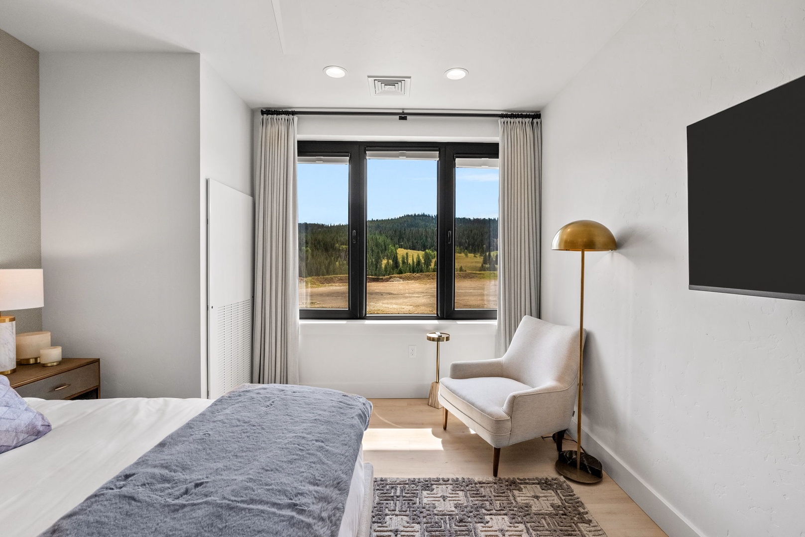 Wake up to stunning mountain scenery framed by your bedroom window. Sunlight streams across plush bedding and warm wood floors, while a cozy reading chair invites you to linger with your morning coffee.