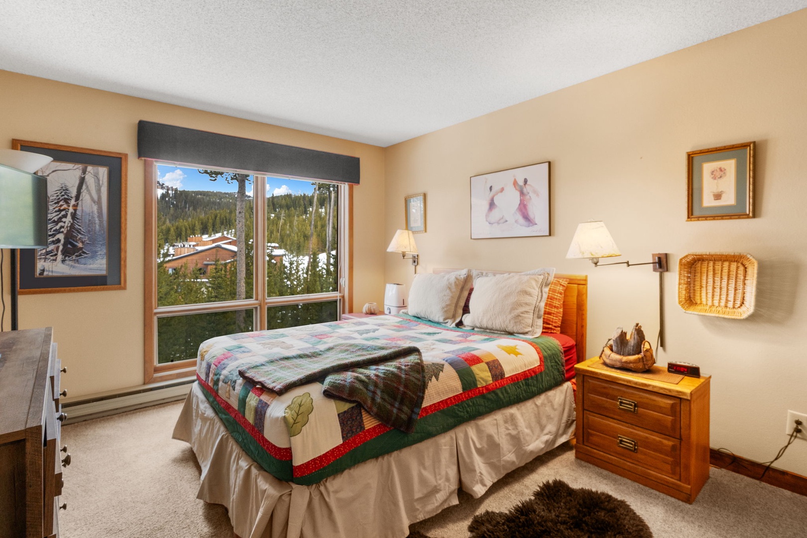 Cozy bedroom with colorful quilt and mountain views through large windows for peaceful nights after your mountain adventures.