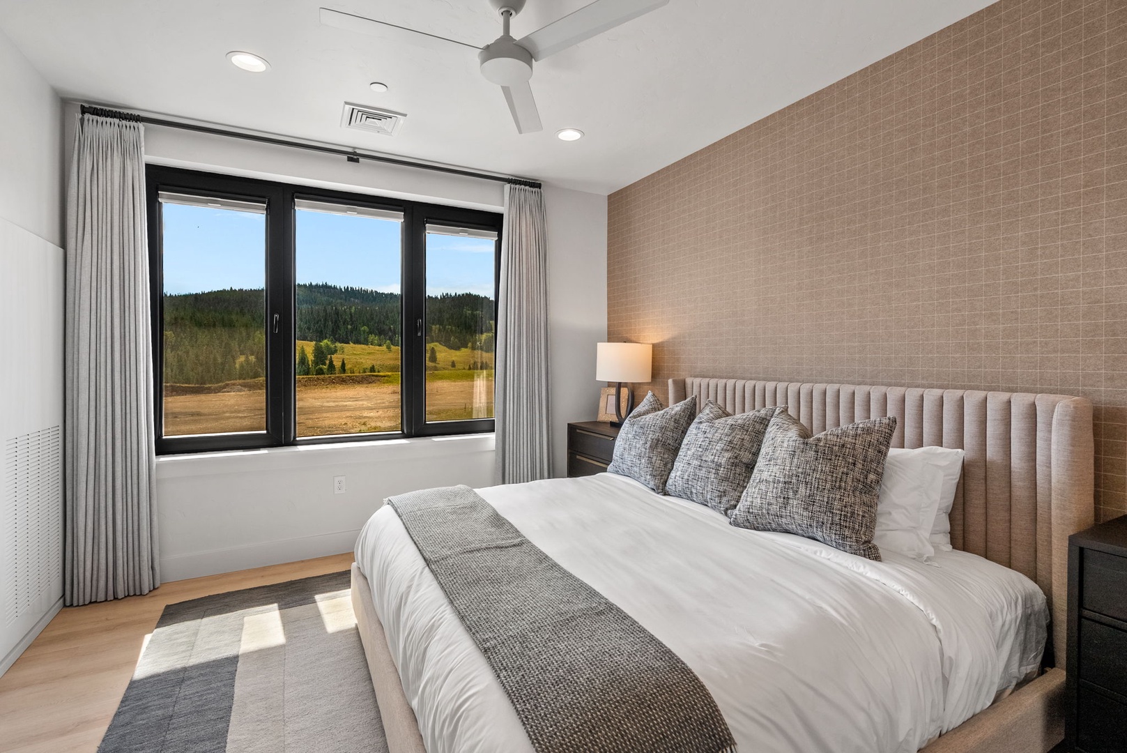 Wake up to sweeping mountain meadow views framed by large windows in your serene, modern bedroom. Soft textures and natural light create a peaceful retreat for restful nights.