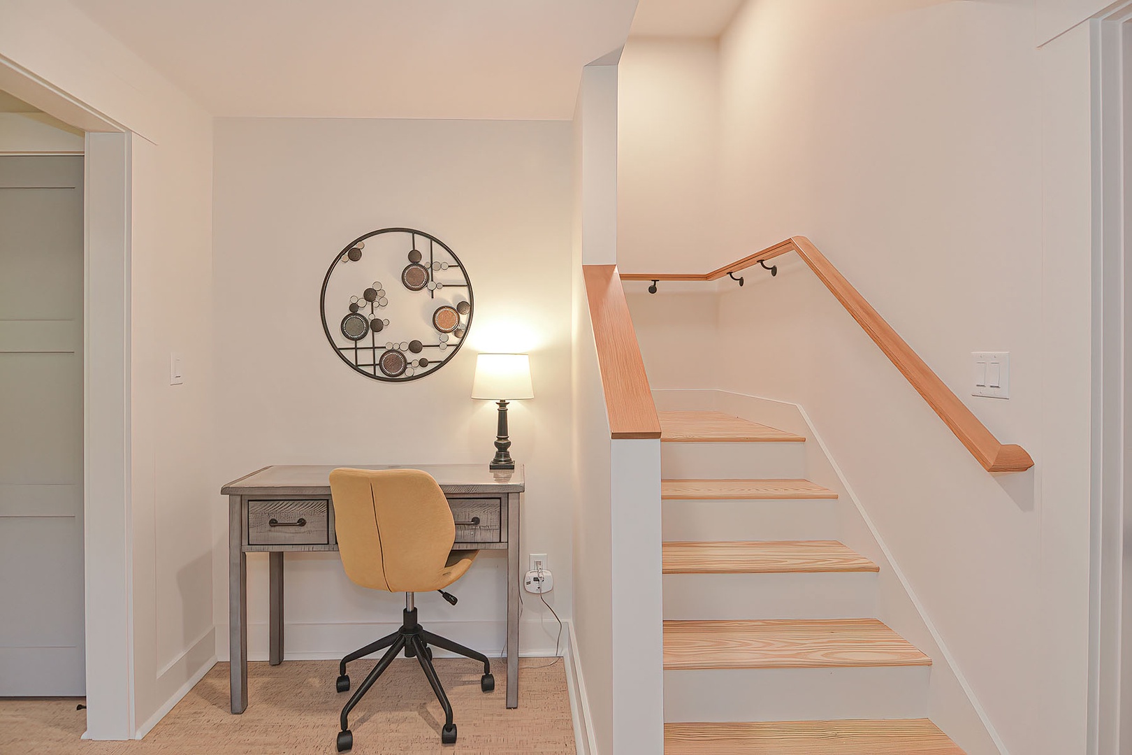 Next to the stairs, there is a snug workstation with a desk, outlets, and a rolling chair.