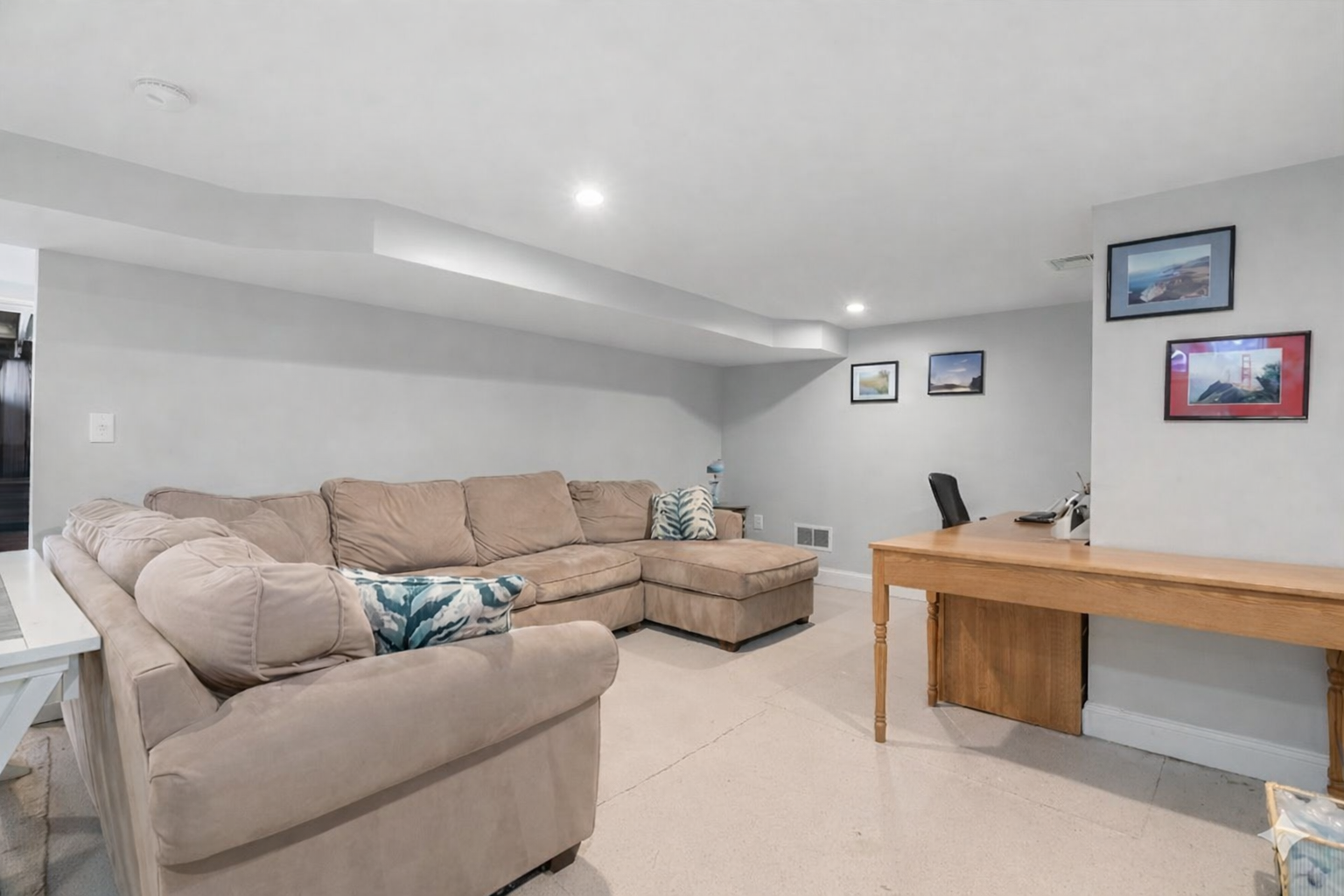 Spacious basement with a large sofa and dedicated desk area.