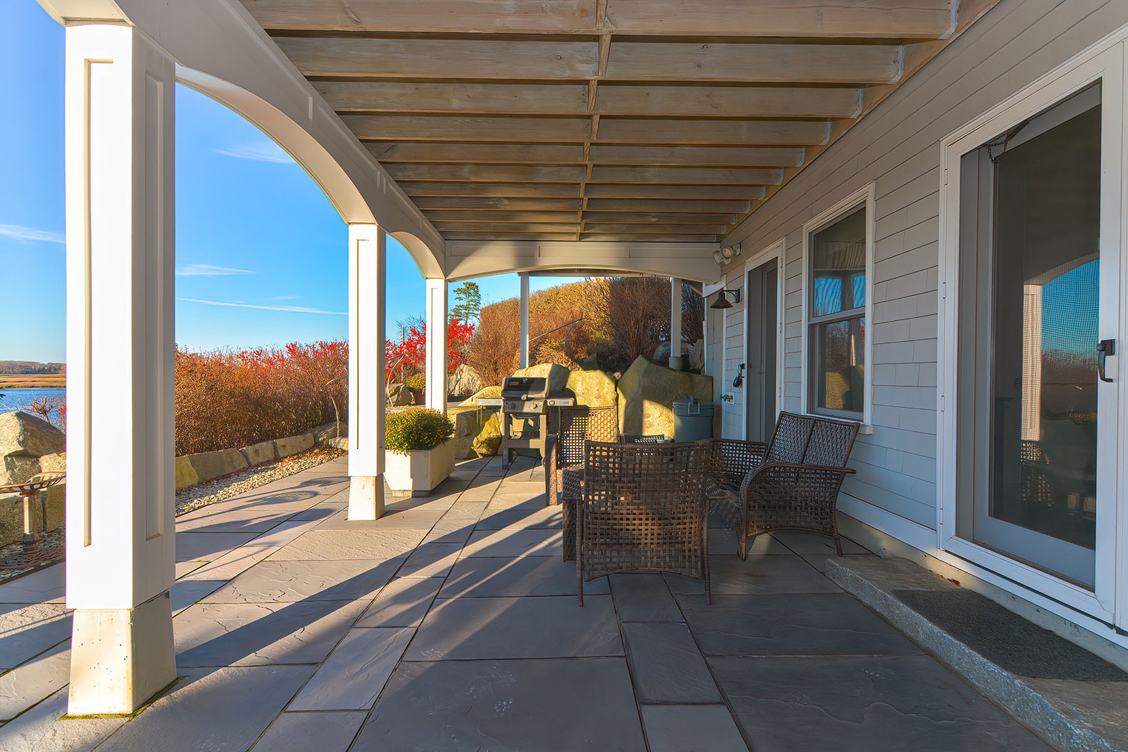 Relax on the covered stone patio with comfortable seating, a grill, and stunning waterfront views.