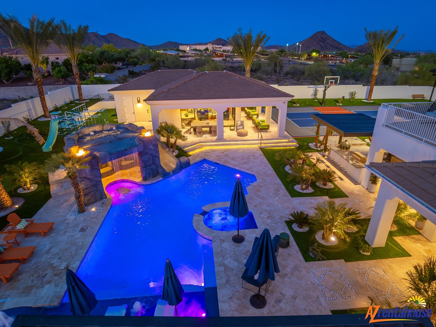 Luxurious desert estate featuring a stunning pool complex with waterfall, spa, and multiple outdoor entertainment areas at twilight.