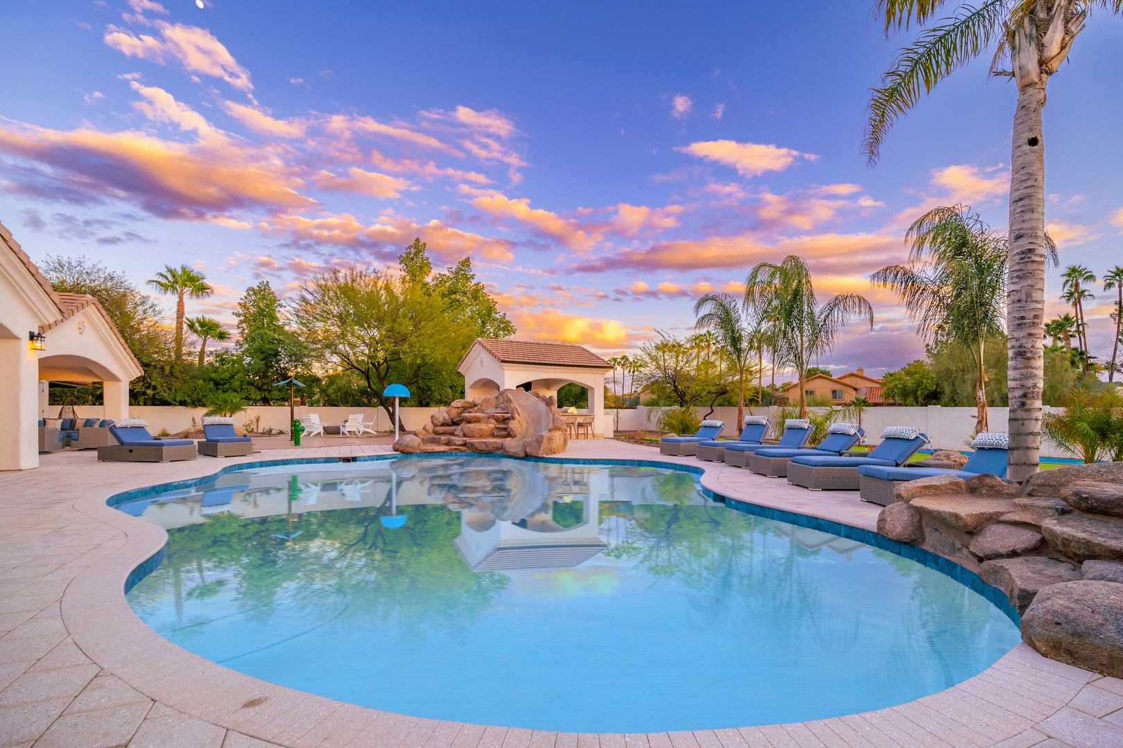 A stunning desert resort pool area framed by swaying palms and dramatic sunset skies, offering a serene escape in the heart of the surrounding neighborhood.
