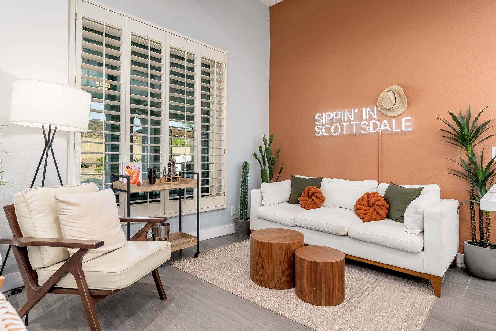 Unwind in your stylish living room with warm terracotta tones, mid-century furnishings, and natural light streaming through plantation shutters, creating your perfect desert oasis.