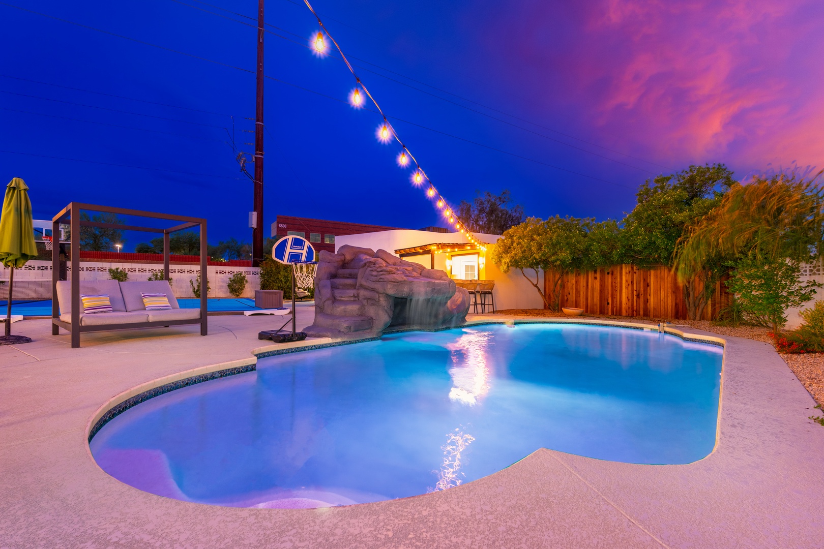 As dusk settles, your private pool glows under twinkling lights, inviting you to unwind beneath desert skies. Lounge poolside, shoot hoops, or soak in the ambiance—this stunning backyard retreat awaits your unforgettable escape.