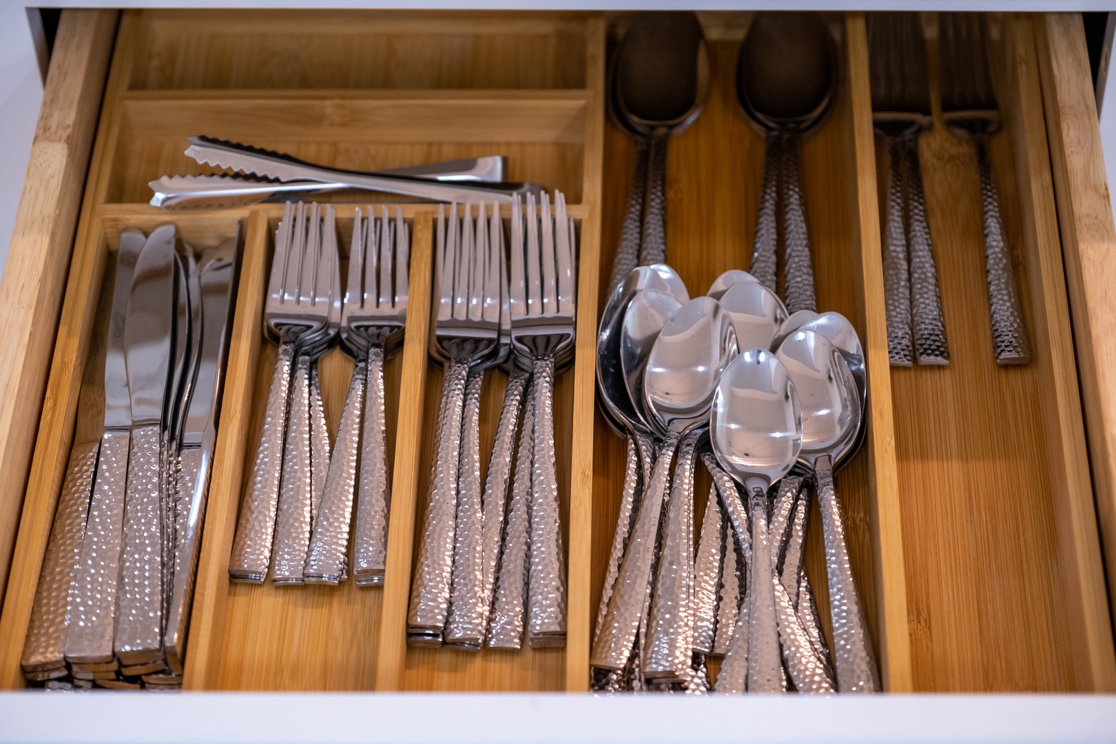 Your fully stocked flatware drawer features elegant utensils with textured metallic handles, perfectly organized and ready for every meal you'll enjoy during your stay.