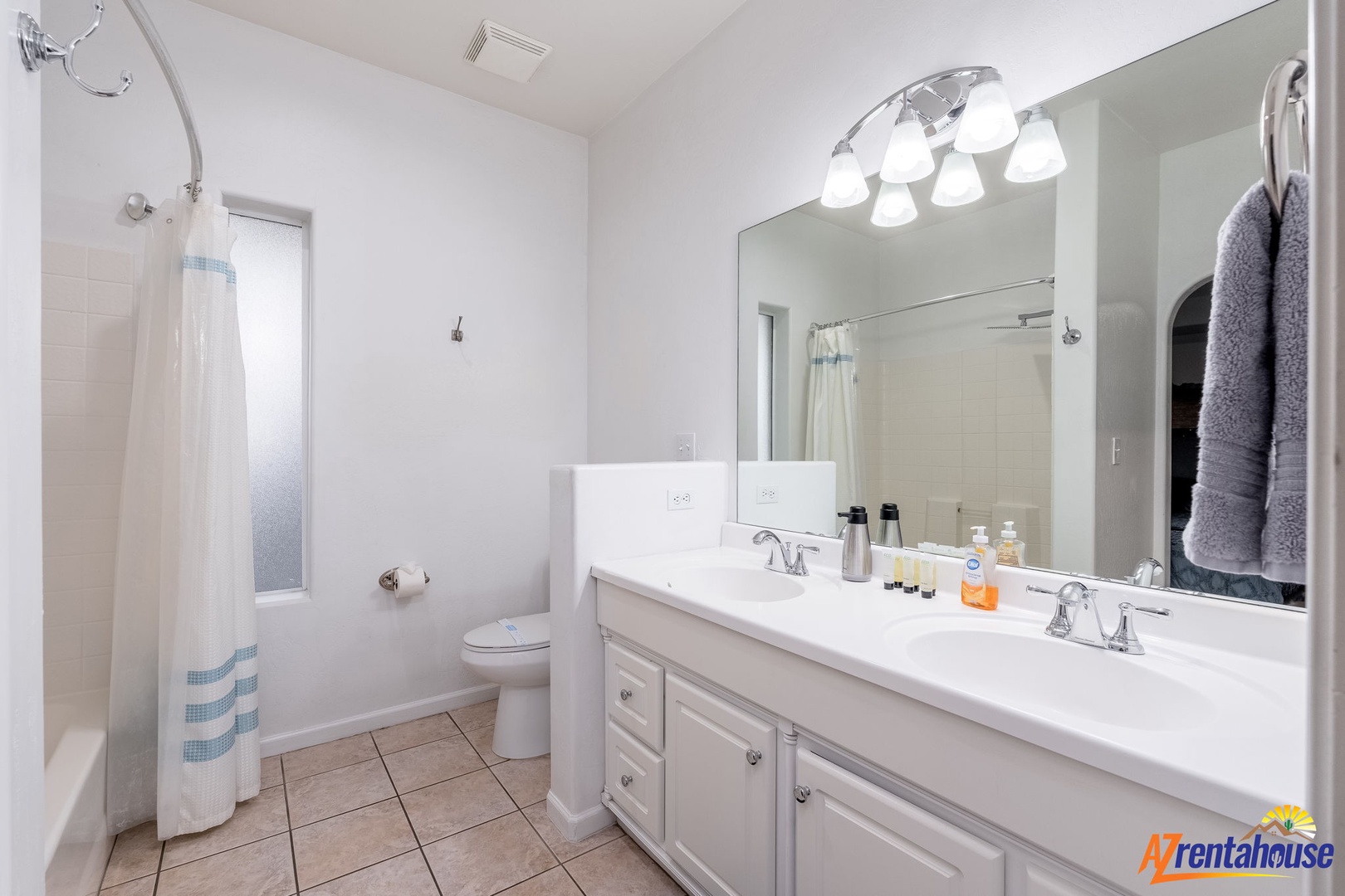 Step into your bright, spotless bathroom with dual sinks, a refreshing shower, and fluffy towels ready for your arrival. Fresh toiletries await at the vanity for your convenience.