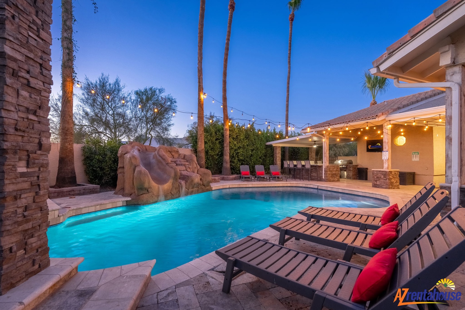 The property features a resort-style pool with decorative rock waterfall, palm trees, and covered outdoor dining area—perfect for Arizona evenings under string lights.
