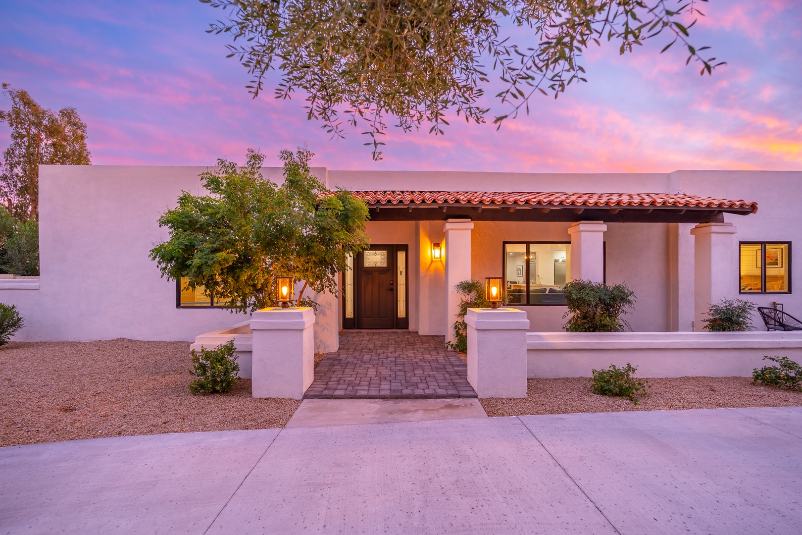 Stunning sunset illuminates this Southwest-style villa, featuring classic tile roofing, pristine white stucco, and warm ambient lighting that welcomes you home after a day of adventure.