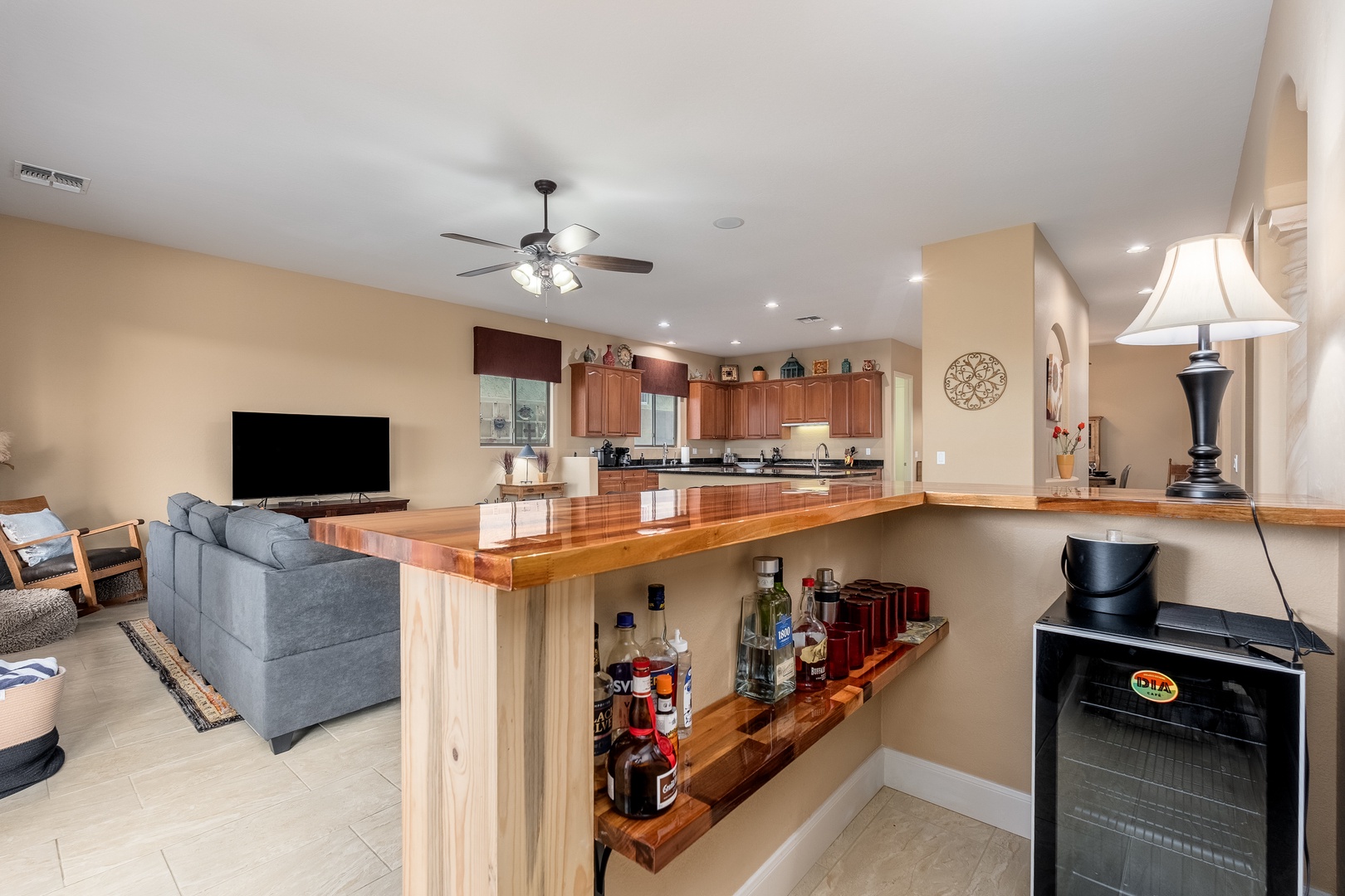 Gather in this open-concept living space featuring a welcoming kitchen, cozy seating area with flat-screen TV, and a custom wooden bar—your perfect spot to relax and entertain.