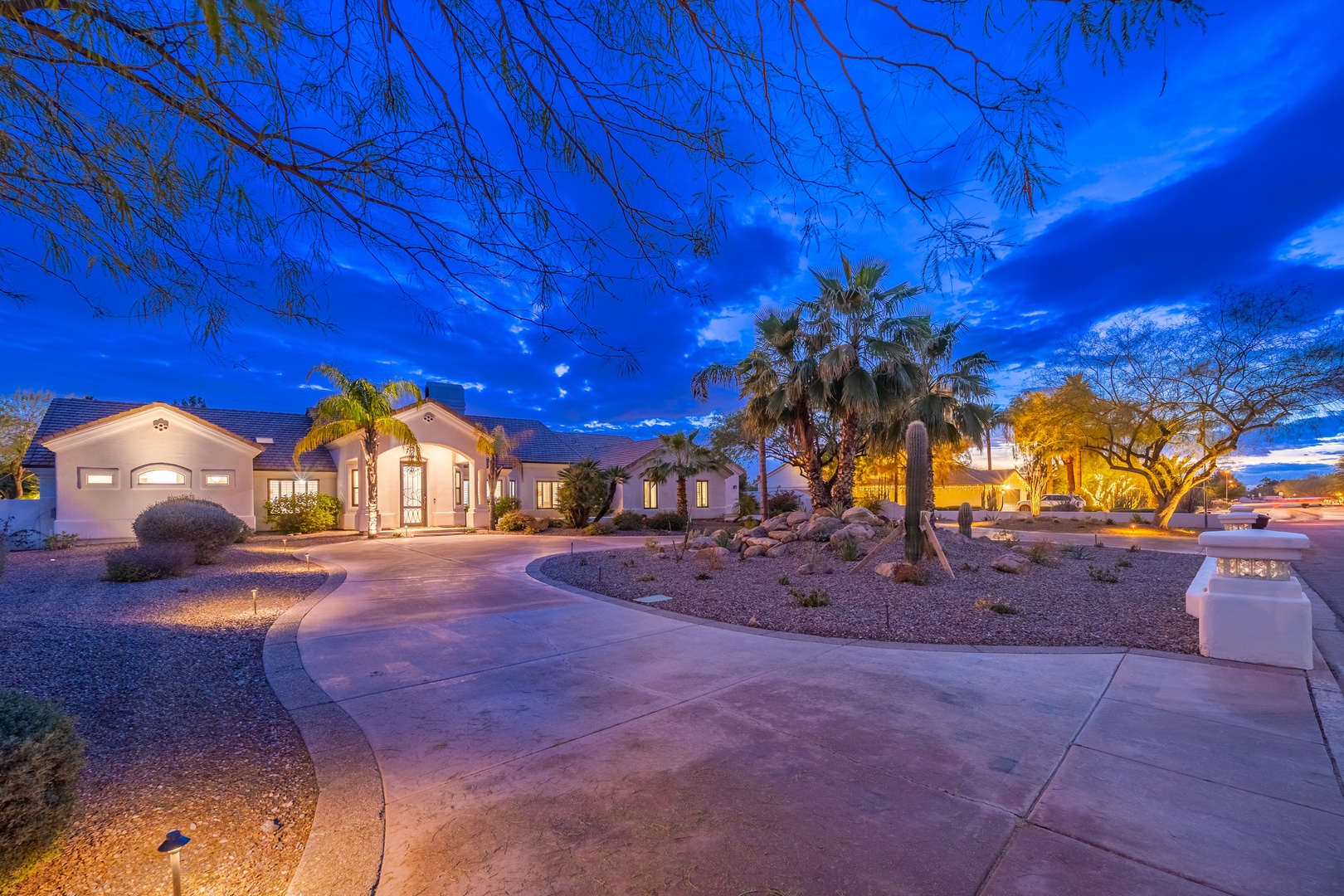 Twilight descends upon the desert property, with palm trees silhouetted against a vibrant blue sky and soft lighting illuminating the southwestern architecture and manicured desert landscaping.