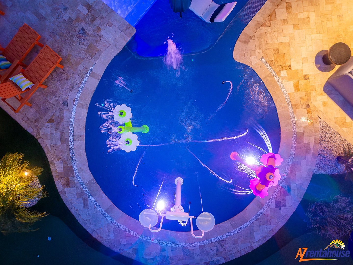 Aerial view of the illuminated swimming pool featuring colorful floating decorations and surrounded by elegant stone decking.