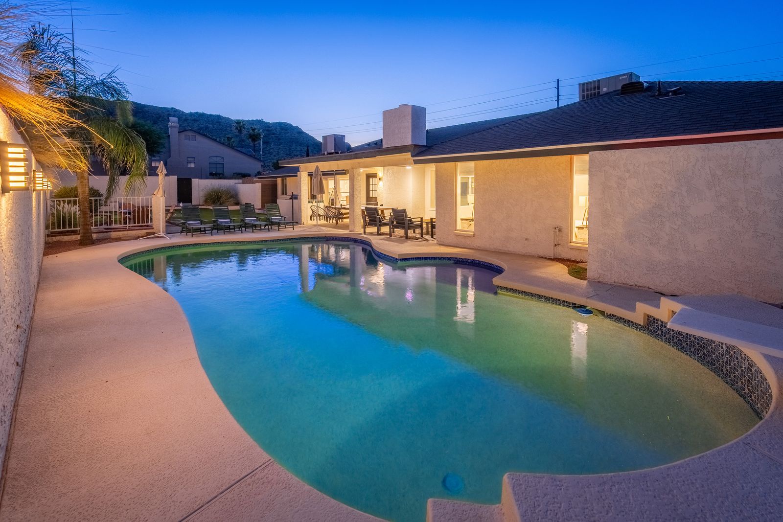 A private desert oasis awaits with a sparkling pool, inviting loungers, and mountain views. Evening lighting creates the perfect ambiance for your sunset swim or poolside relaxation under the stars.