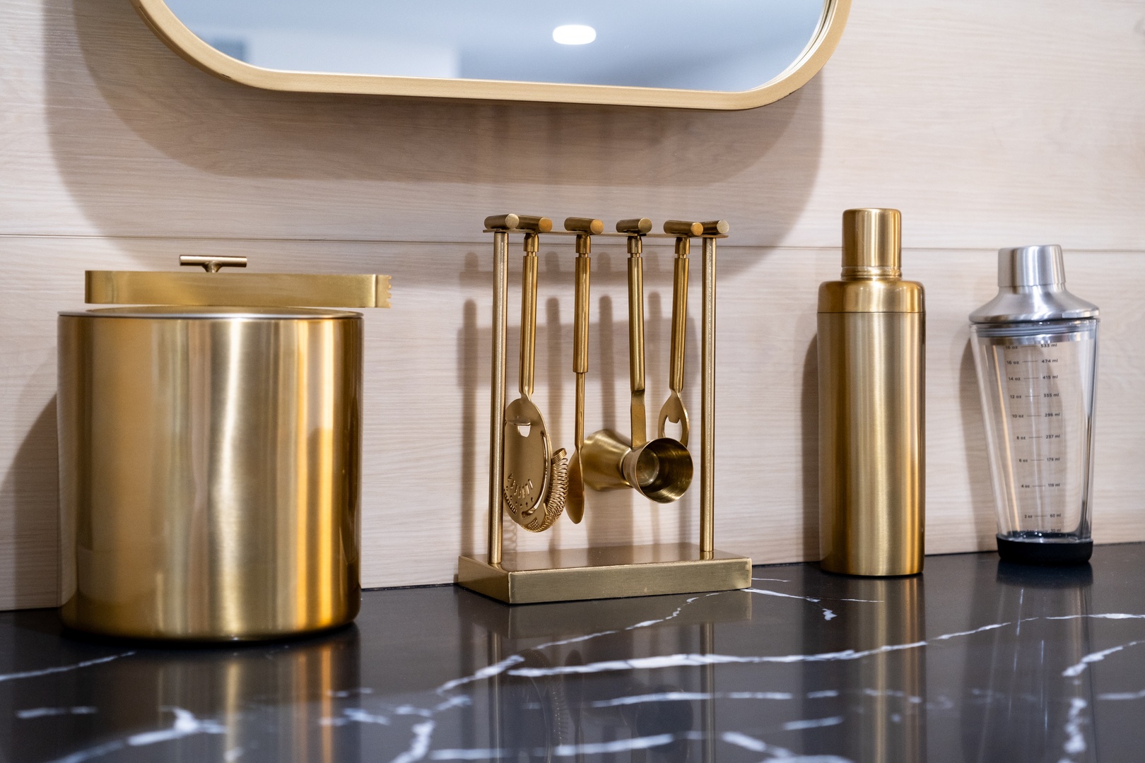 Mix your favorite cocktails with elegant barware featuring a sleek ice bucket, professional cocktail shaker, and gold bar tools on a polished counter beneath a chic mirror.