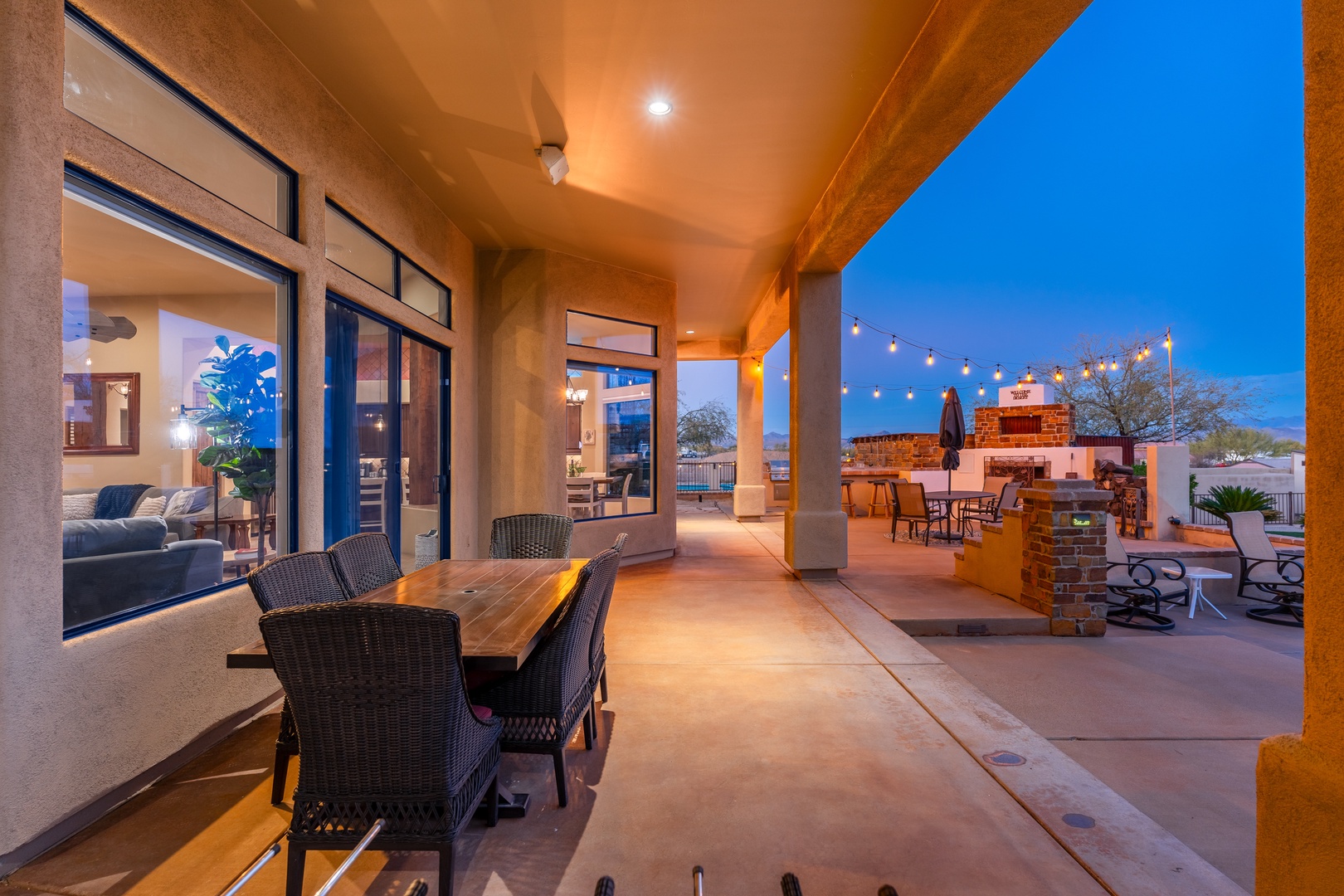An elegant covered patio invites you to dine al fresco beneath warm lighting and starlit skies, with a cozy outdoor fireplace completing the atmosphere.