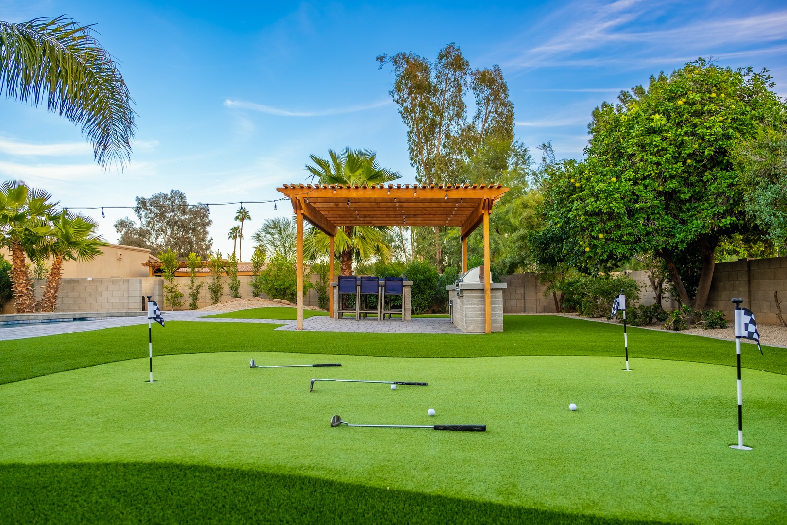 A spacious backyard features a private miniature golf course surrounded by lush palms and mature trees, with a pergola-covered seating area perfect for outdoor gatherings.