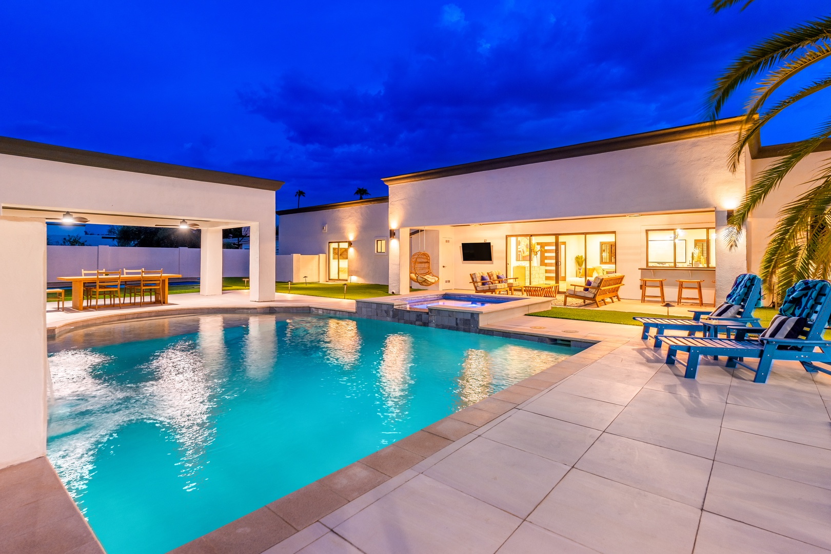 A stunning modern estate captured at twilight reveals a pristine pool surrounded by spacious patio areas, elegant outdoor dining, and welcoming interiors—perfect for memorable gatherings and relaxation.
