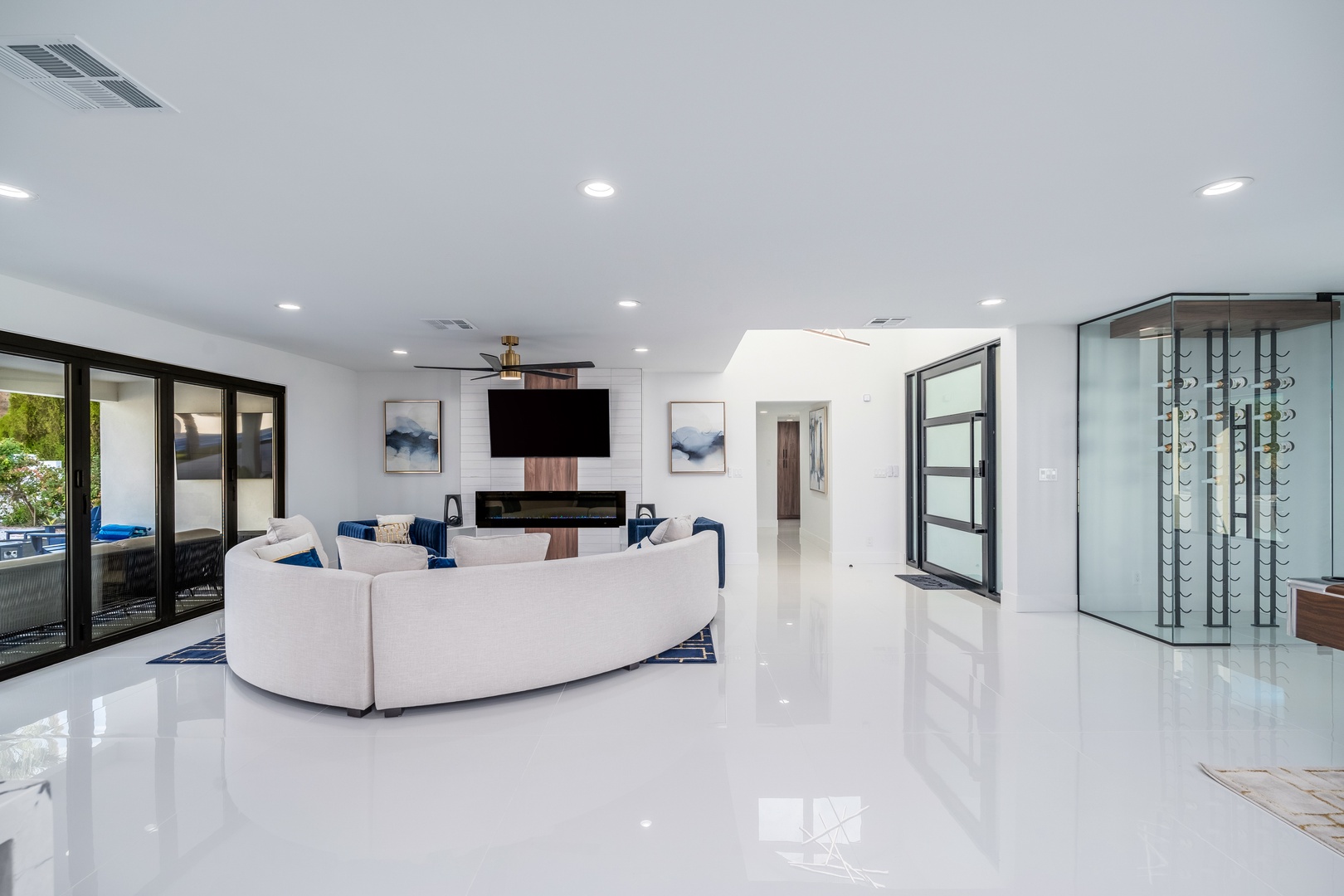 Your open-concept living space features sleek white floors, a curved sectional sofa, and modern fireplace beneath a mounted TV. Natural light streams through patio doors, inviting relaxation.