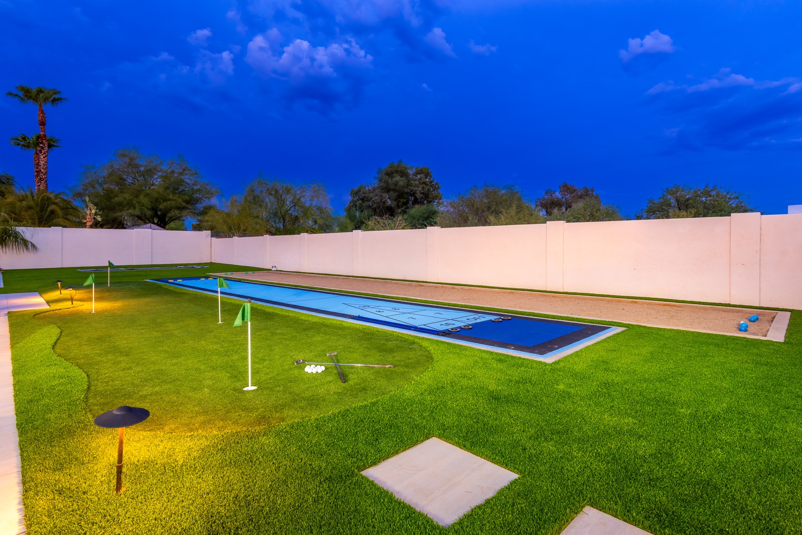 The property features a pristine lap pool and private putting green set within manicured grounds, surrounded by mature trees and evening lighting beneath open desert skies.
