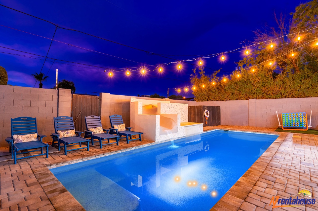 Your private backyard oasis glows under string lights, with a sparkling pool and cozy lounge chairs perfect for evening relaxation.