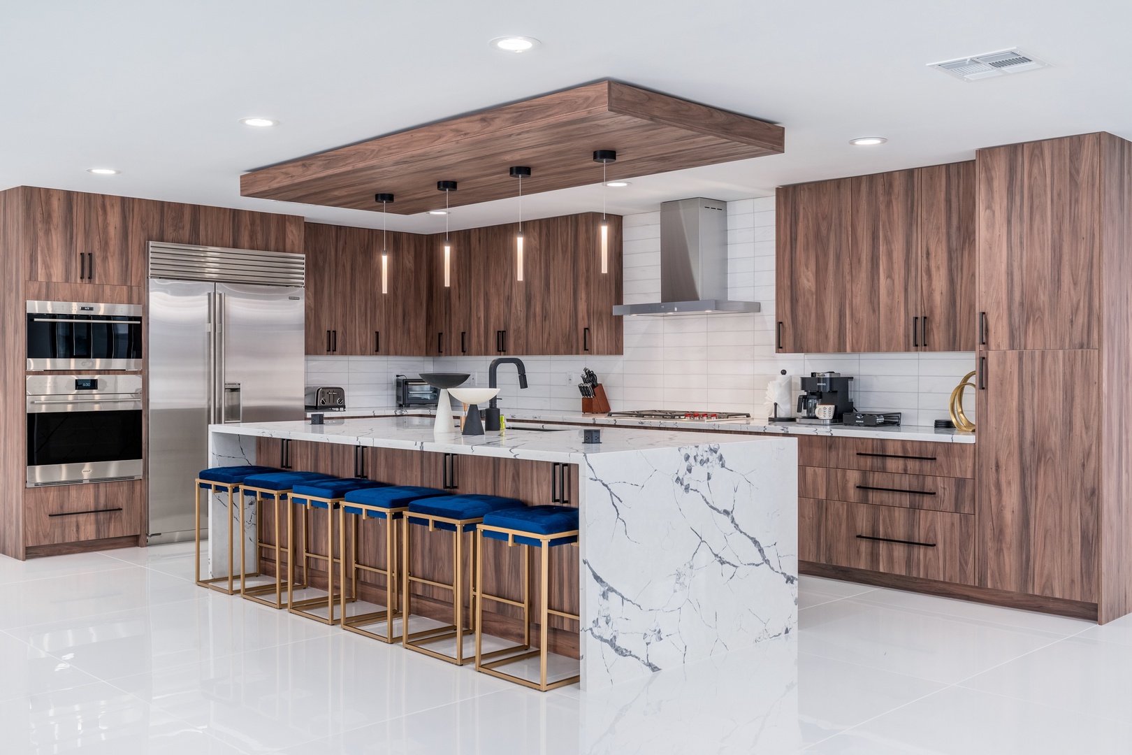 Stunning modern kitchen with sleek marble island, premium appliances, and elegant blue-cushioned seating invites you to whip up memorable meals or gather for morning coffee.