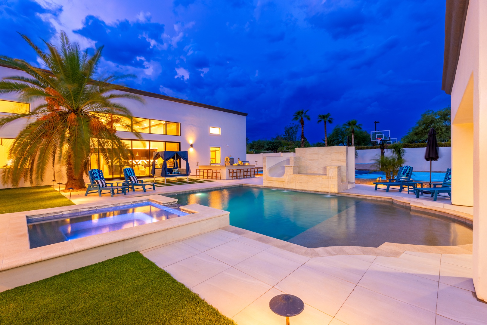 Modern luxury estate features a stunning pool, hot tub, and outdoor entertaining spaces beneath dramatic evening skies—perfect for gathering and relaxation.