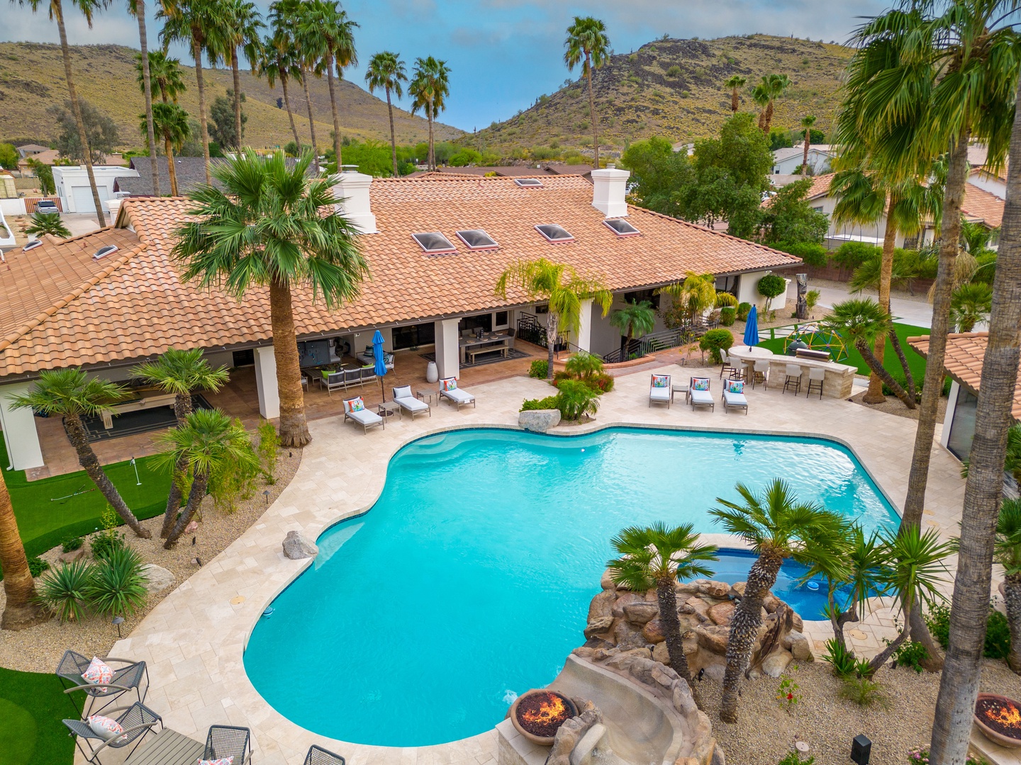 Desert retreat with Spanish-tiled villa featuring a stunning pool, palm trees, and mountain views. The property sits in a peaceful neighborhood surrounded by natural desert landscape.