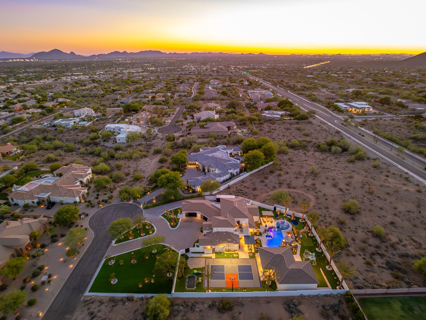 Aerial view of the property's desert neighborhood at sunset, showcasing the surrounding area with mountain backdrop and spacious residential setting.