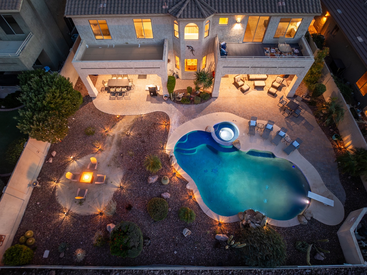 This stunning property features a custom pool, hot tub, multiple outdoor seating areas, and beautifully landscaped surroundings, all bathed in the warm glow of evening lighting.