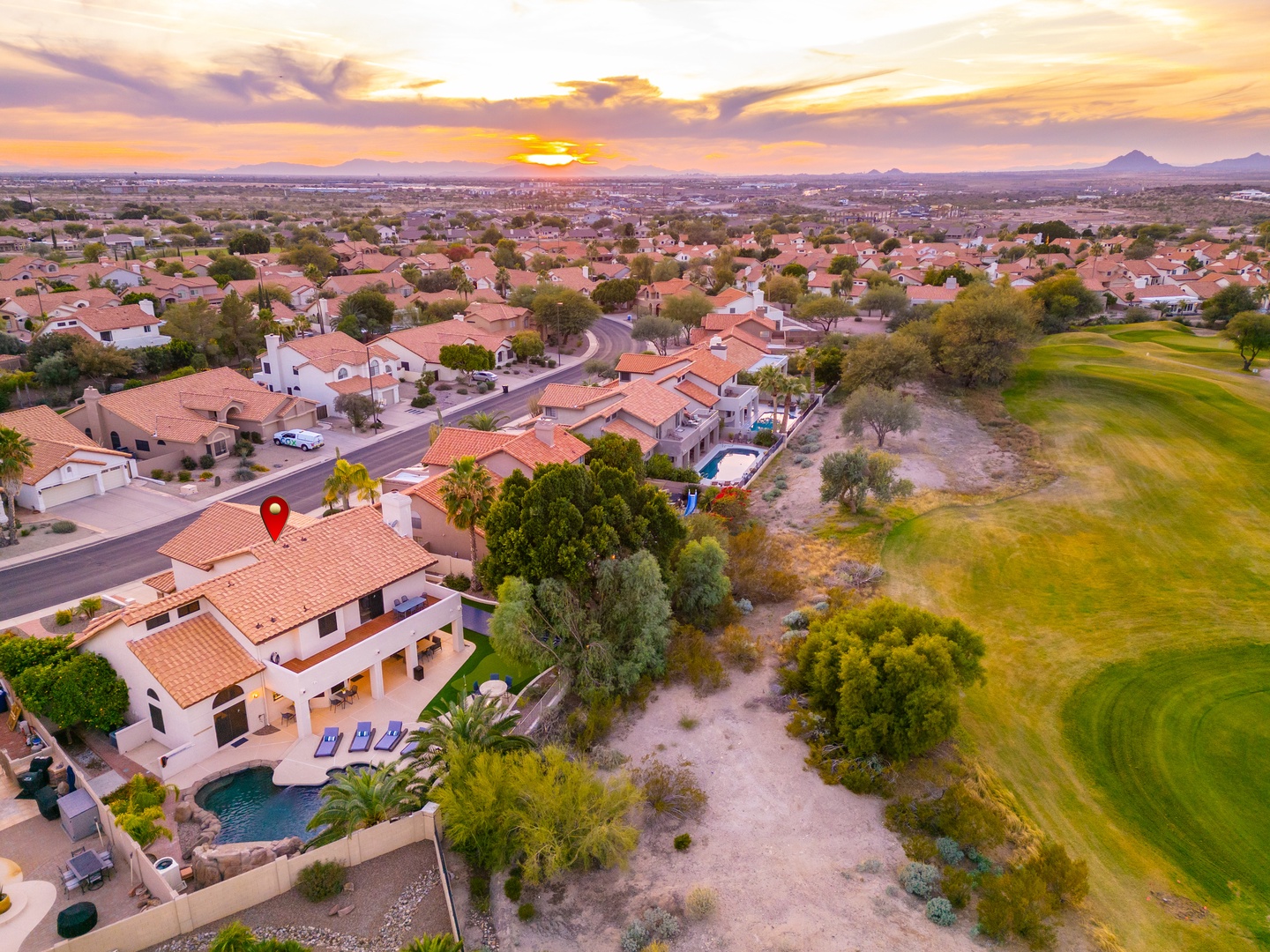 Aerial view of an elegant southwestern-style villa featuring a private pool, landscaped grounds, and positioned alongside a lush golf course within a serene residential neighborhood at sunset.