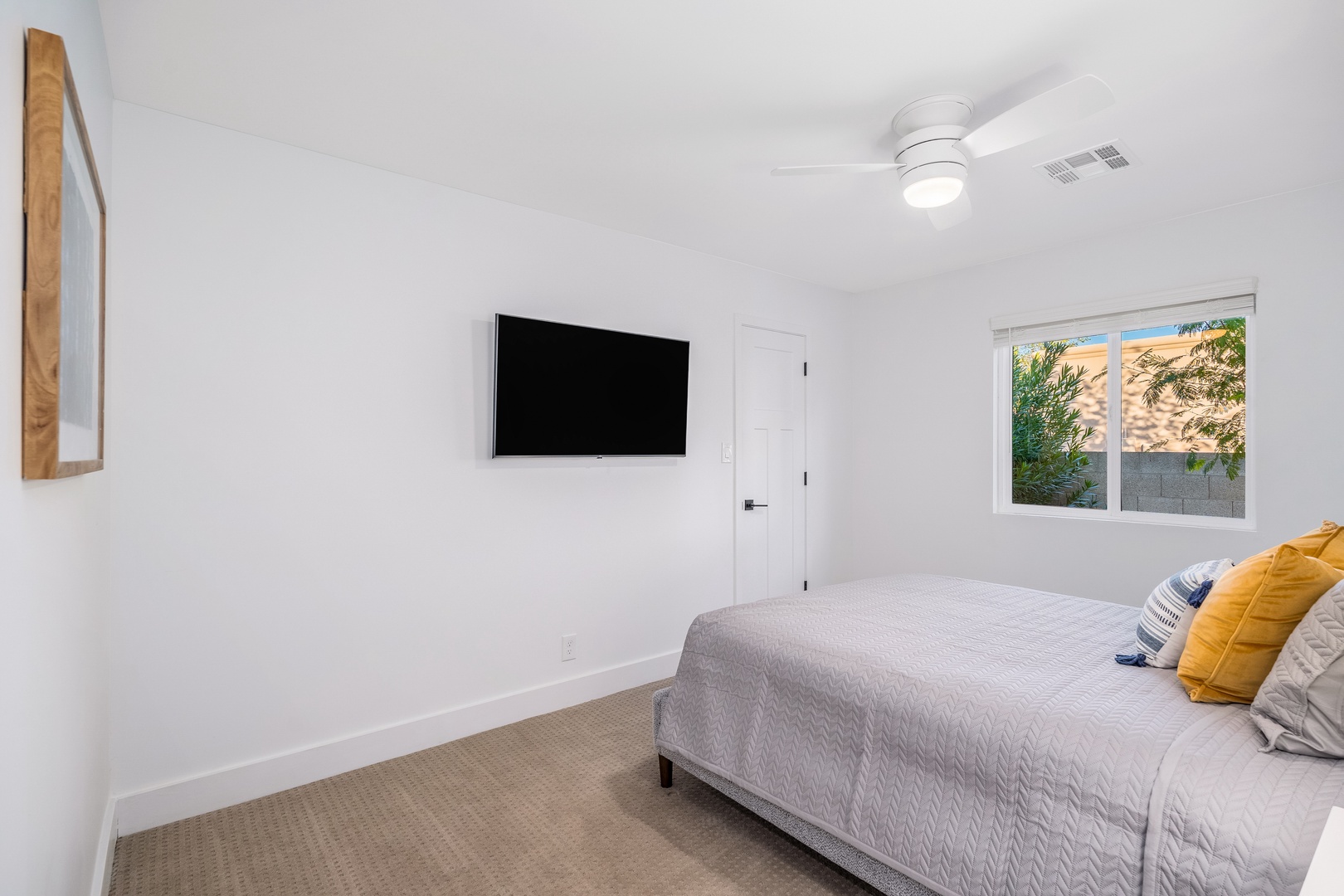 Your peaceful bedroom retreat features soft carpeting, a wall-mounted TV for your entertainment, and natural light streaming through the window. The ceiling fan keeps you comfortable year-round.