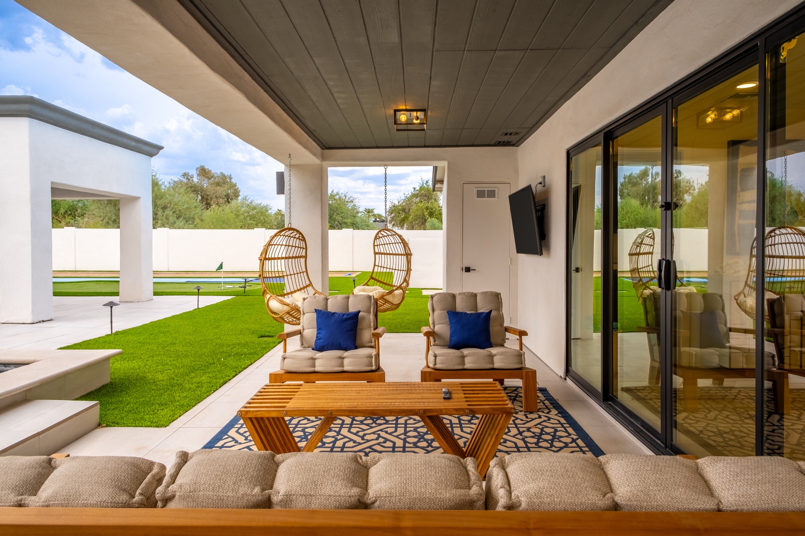 Unwind in your private covered patio with plush seating, a stylish rug, and lush green lawn views beyond. Unique hanging chairs add a playful touch to your outdoor retreat.