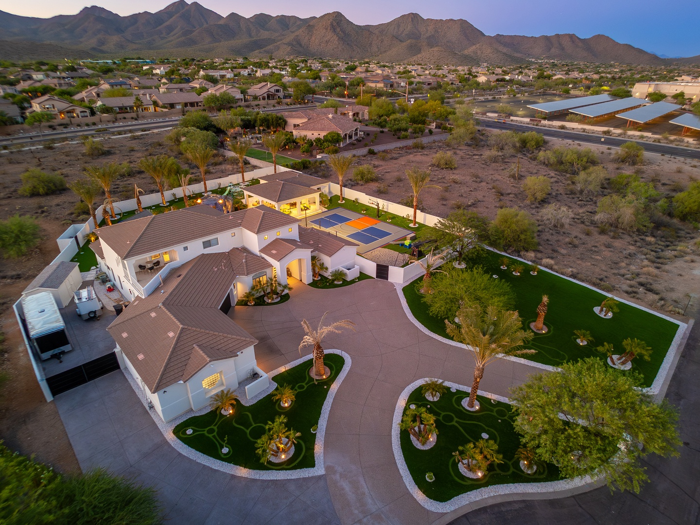Aerial view of a spacious desert property featuring landscaped grounds, outdoor recreation areas, and dramatic mountain backdrop in a tranquil neighborhood setting.