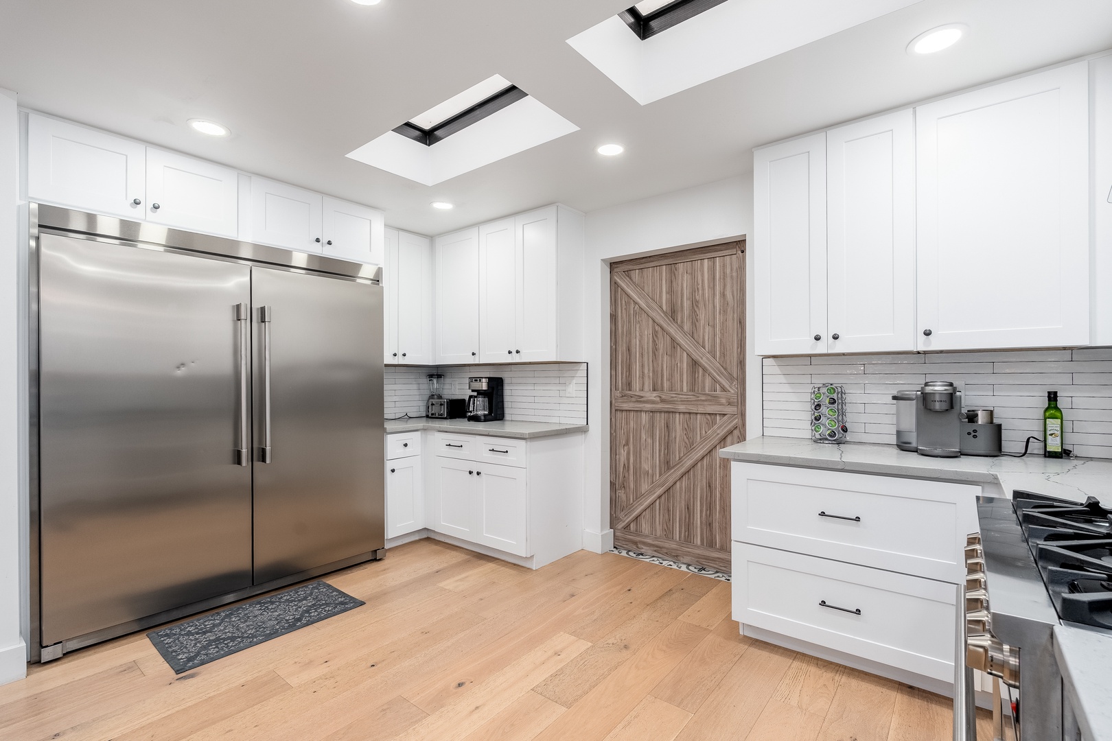Your culinary retreat awaits with gleaming stainless-steel appliances, sleek white cabinetry, and sun-drenched skylights overhead. Light hardwood floors and modern fixtures create a bright, welcoming space for crafting memorable meals.